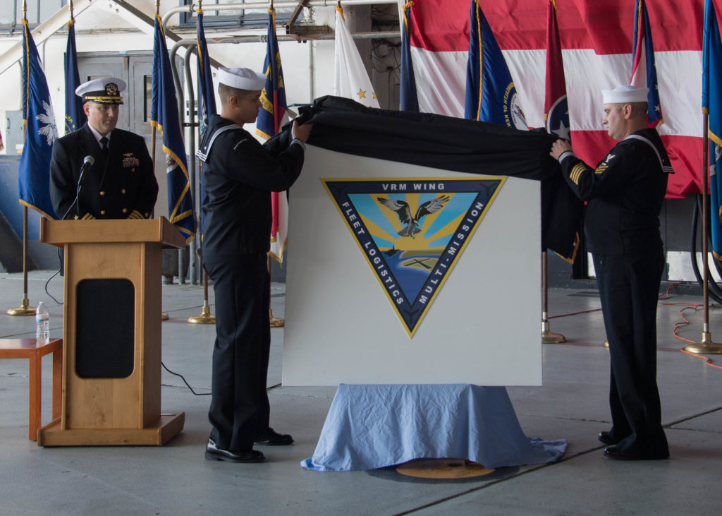 Los marinos asignados a Fleet Logistics Multi-Mission Wing (COMVRMWING) 1 descubren el logotipo del Ala en la ceremonia celebrada en la Estación Aérea Naval de la Isla Norte (NASNI), 