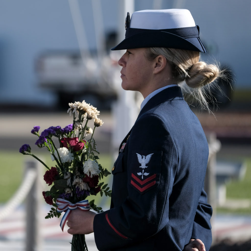 Petty Officer 2nd Class Kristin Archard, an aviation maintenance technician at Coast Guard Air Station Sacramento, holds flowers as she participates in the honor platoon during a remembrance ceremony, Oct. 29, 2019, for fallen aircrews for the 10th anniversary of an aircraft collision between a Coast Guard HC-130 Hercules aircraft and a Marine Corps AH-1 Super Cobra helicopter. 