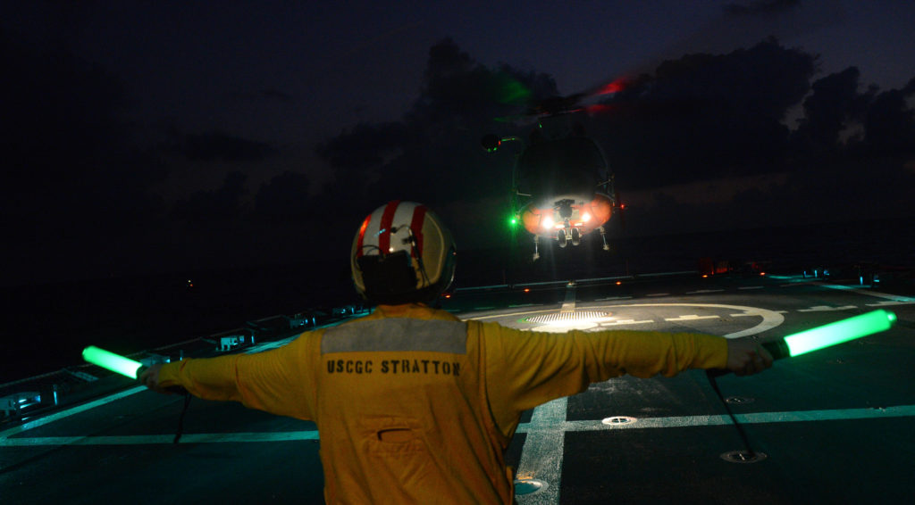 Ens. Olivia Calabro, landing signal officer aboard Coast Guard Cutter Stratton, signals an MH-65 Dolphin helicopter pilot. 