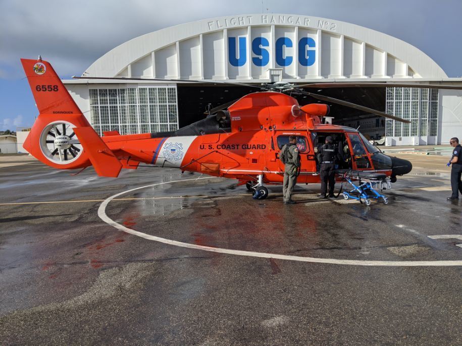 The crew of a Coast Guard Air Station Borinquen MH-65 Dolphin helicopter transfers a rescued man to Emergency Medical Service personnel at Air Station Borinquen Dec. 11, 2019.   The man was transported to a local hospital after high breaking surf knocked him into the water from the jagged edge rocks at Domes Beach in Rincon, Puerto Rico, from where he was able to climb back onto the rocks until his rescue