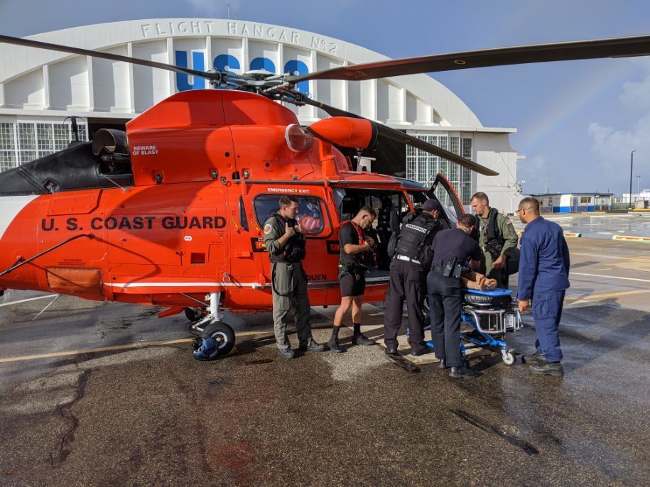 The crew of a Coast Guard Air Station Borinquen MH-65 Dolphin helicopter transfers a rescued man to Emergency Medical Service personnel at Air Station Borinquen Dec. 11, 2019.   The man was transported to a local hospital after high breaking surf knocked him into the water from the jagged edge rocks at Domes Beach in Rincon, Puerto Rico, from where he was able to climb back onto the rocks until his rescue