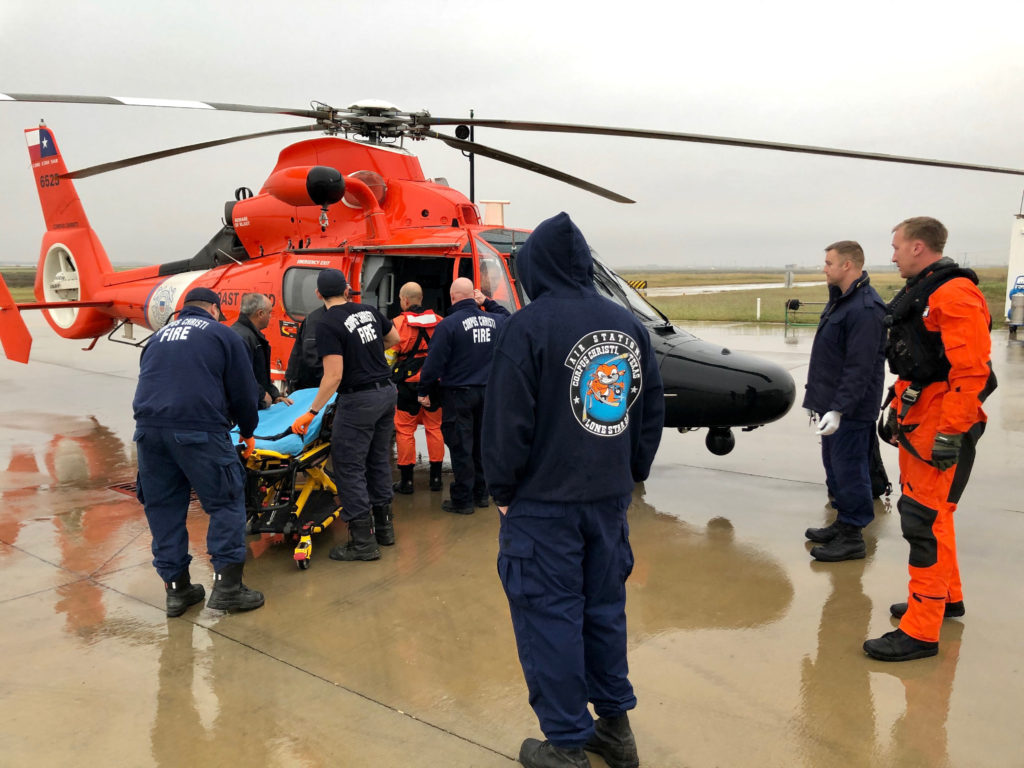 An Air Station Corpus Christi MH-65 Dolphin helicopter aircrew transfers an injured offshore vessel crewmember to awaiting emergency medical services personnel at Sector/Air Station Corpus Christi, Texas, Dec. 20, 2019. The 20-year-old male crewmember injured his leg while conducting operations aboard the offshore vessel Ram XVII.  