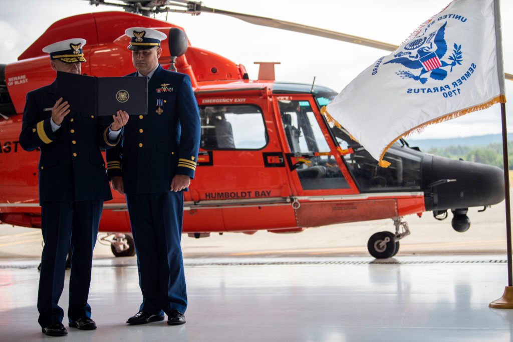 Rear Adm. Brian Penoyer, Eleventh Coast Guard District commander,??presents the Distinguished Flying Cross to Cmdr. Derek Schramel, a Coast Guard Air Station Humboldt Bay MH-65 Dolphin helicopter pilot, Aug. 6, 2020 in Humboldt Bay, California. 